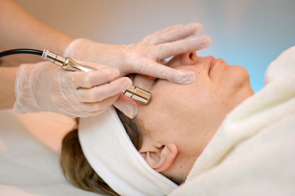 gloved hands performing microdermabrasion on womans face