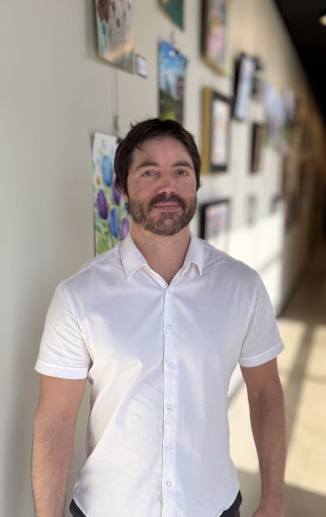 Lee, a Precision Wellness provider, standing in a bright hallway wearing a white button-up shirt.