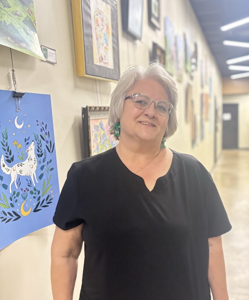 Provider smiling in a bright hallway at Precision Wellness, wearing glasses and a black top with colorful artwork in the background.