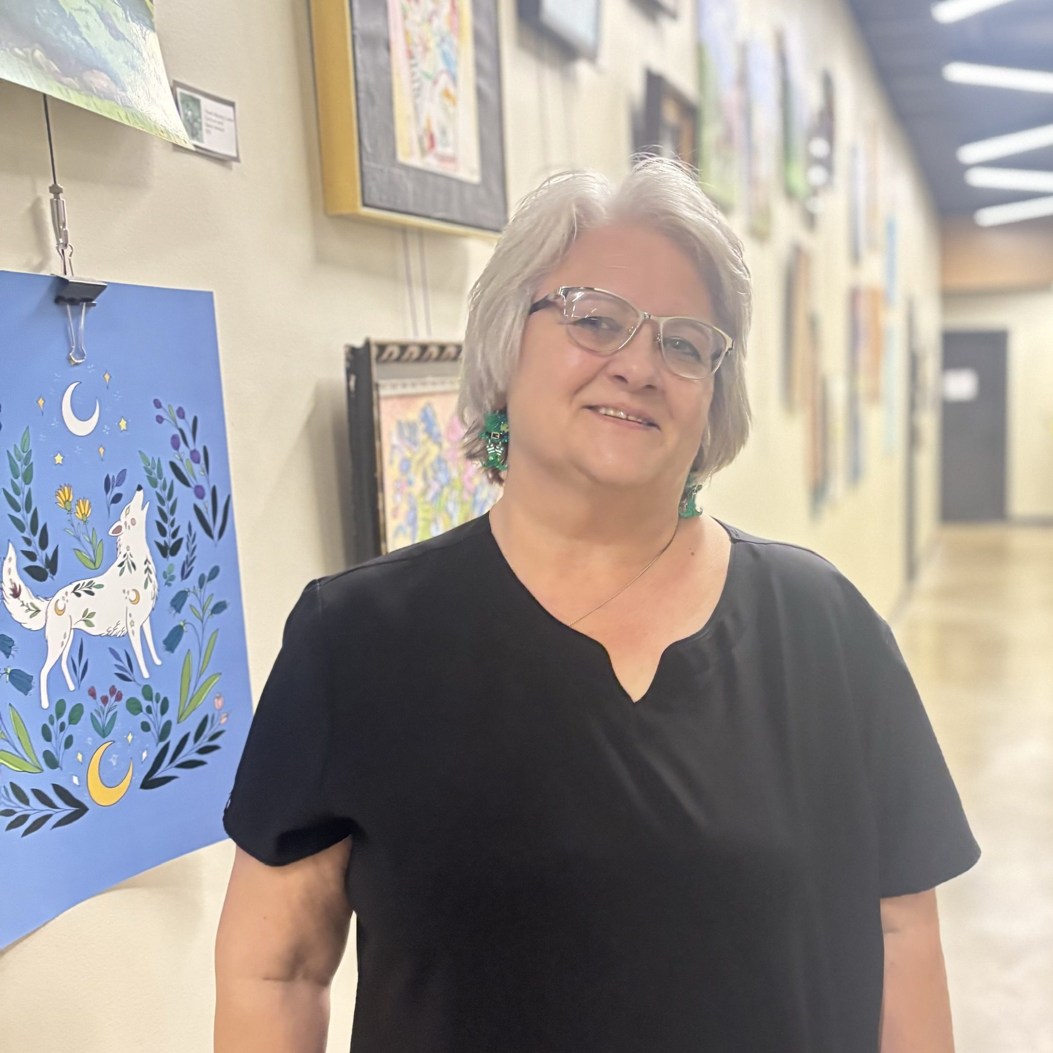 Provider smiling in a bright hallway at Precision Wellness, wearing glasses and a black top with colorful artwork in the background.