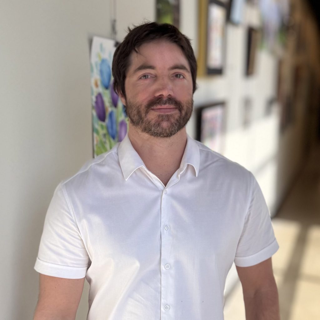 Lee, a Precision Wellness provider, standing in a bright hallway wearing a white button-up shirt.