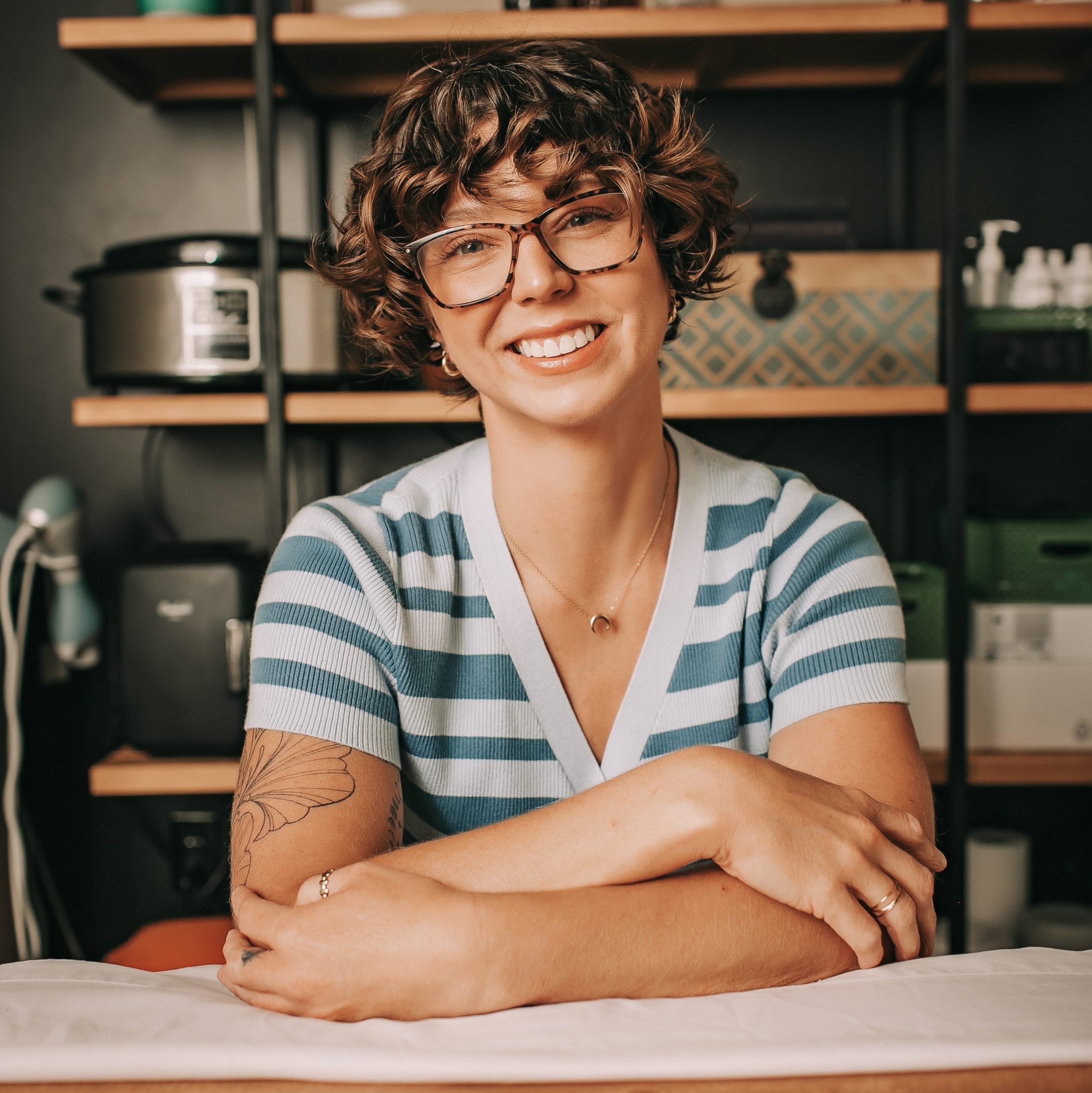 Jenny Gabris smiling in a treatment room, wearing glasses and a blue-and-white striped top.