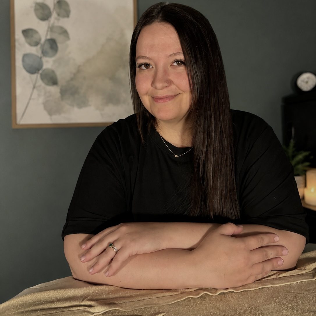 Dakota Upp, LMT, smiling in a treatment room at Precision Wellness, leaning on a massage table.
