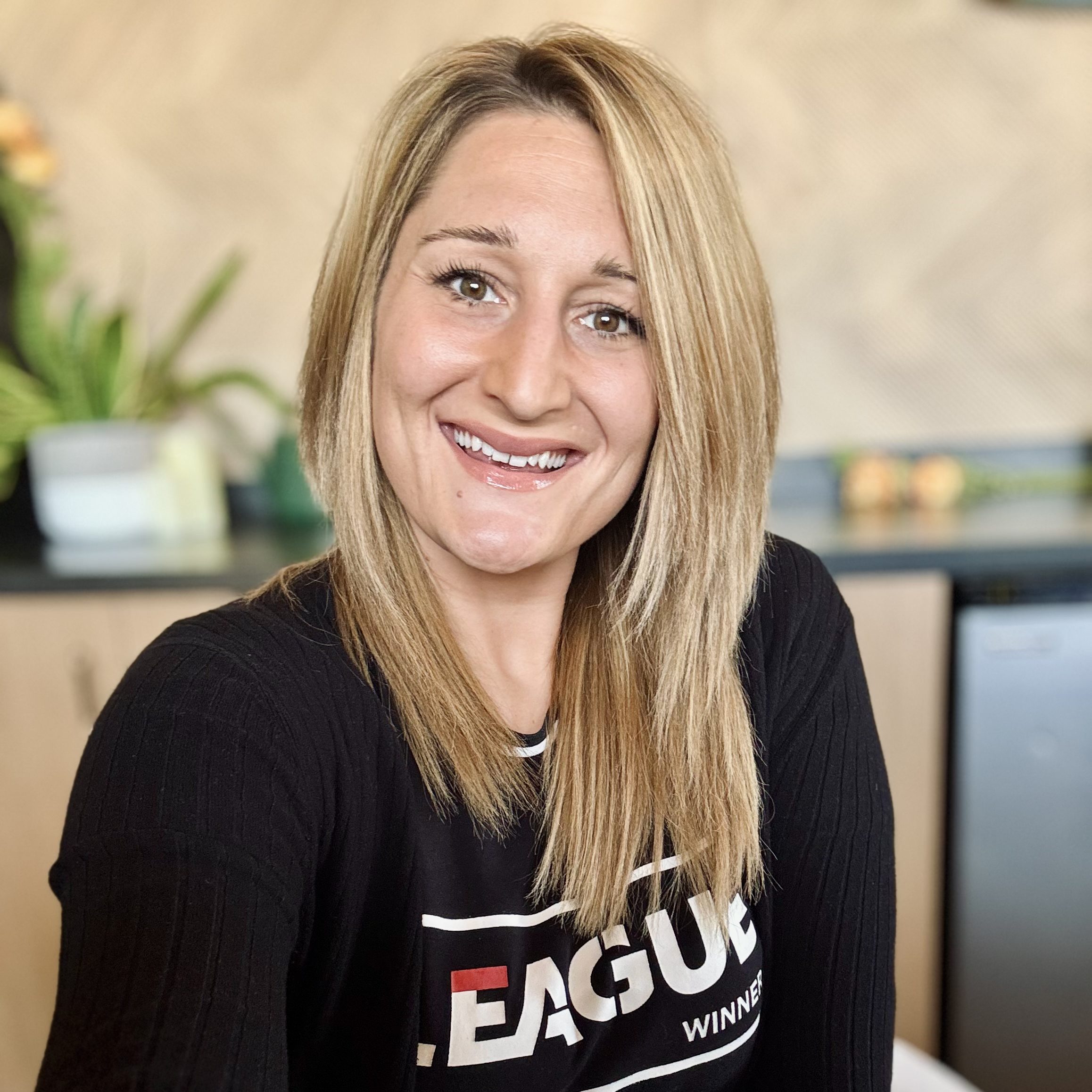 Kristina Dodd smiling in a treatment room at Precision Wellness, wearing a black top with a softly blurred background.